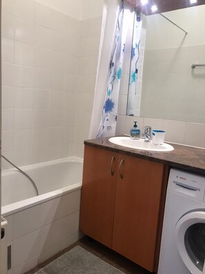 Een badkamer met een bad, een wastafel met spiegel en een wasmachine.