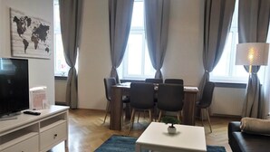 A modern living room with a TV, a small table, a sofa, and a dining area with chairs and a table. - Wohnung in Hernals (Wien)