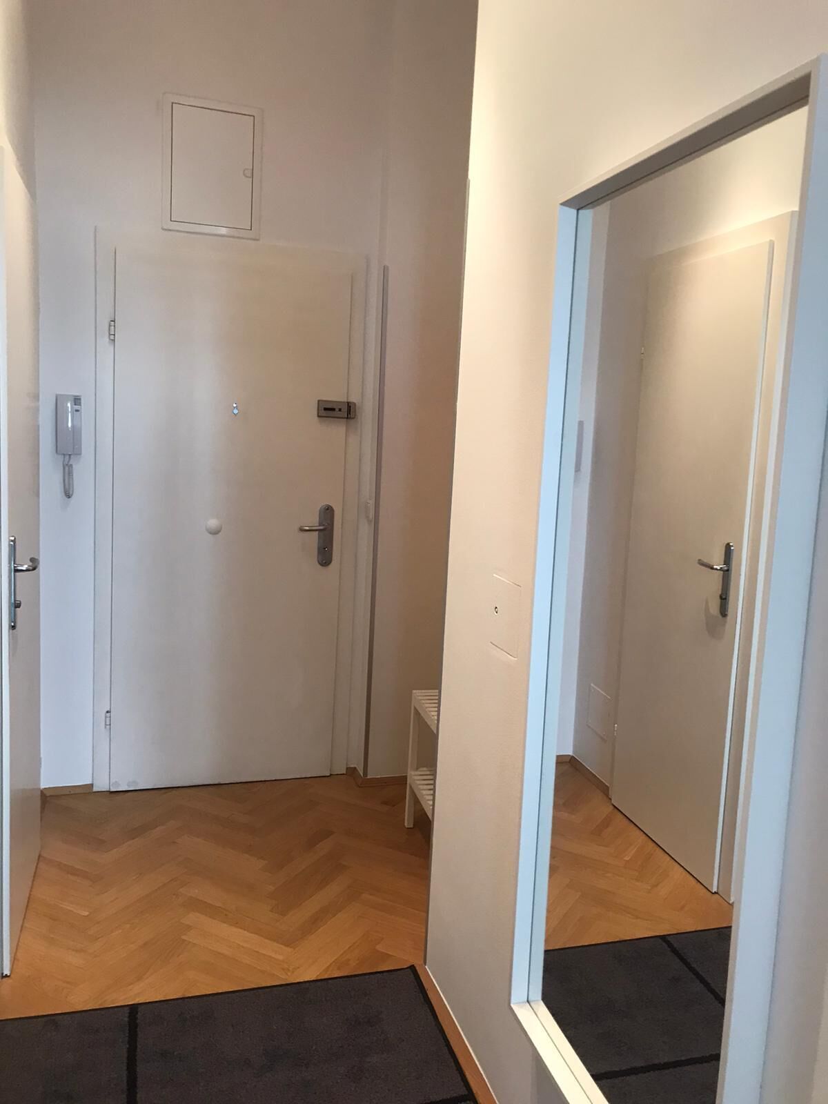 Un passadís amb terra de fusta, parets blanques i una porta amb una petita estant.
