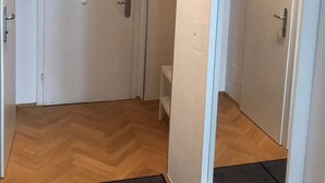 A hallway with a wooden floor, white walls, and a door with a small shelf. - Wohnung in Hernals (Wien)