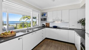 A modern kitchen with white cabinets, a black countertop, and a view of the ocean. - Stunning Beach Views With Pool. Easy Walk To Beach (KILLCARE)