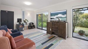 A modern living room with a fireplace, a large TV, and a view of the ocean through large windows. - Stunning Beach Views With Pool. Easy Walk To Beach (KILLCARE)