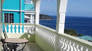 A covered outdoor area with a table and chairs, a view of the sea, and a blue building in the background. - 5 Mins from beach! (Mero)