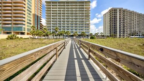 Un muelle que conduce a un gran hotel con varios pisos y balcones, rodeado de zonas verdes y palmeras.