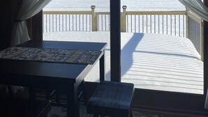 A wooden deck with a table and chairs, overlooking a snowy landscape. - Cozy cabin steps from the lake! (Brainerd)