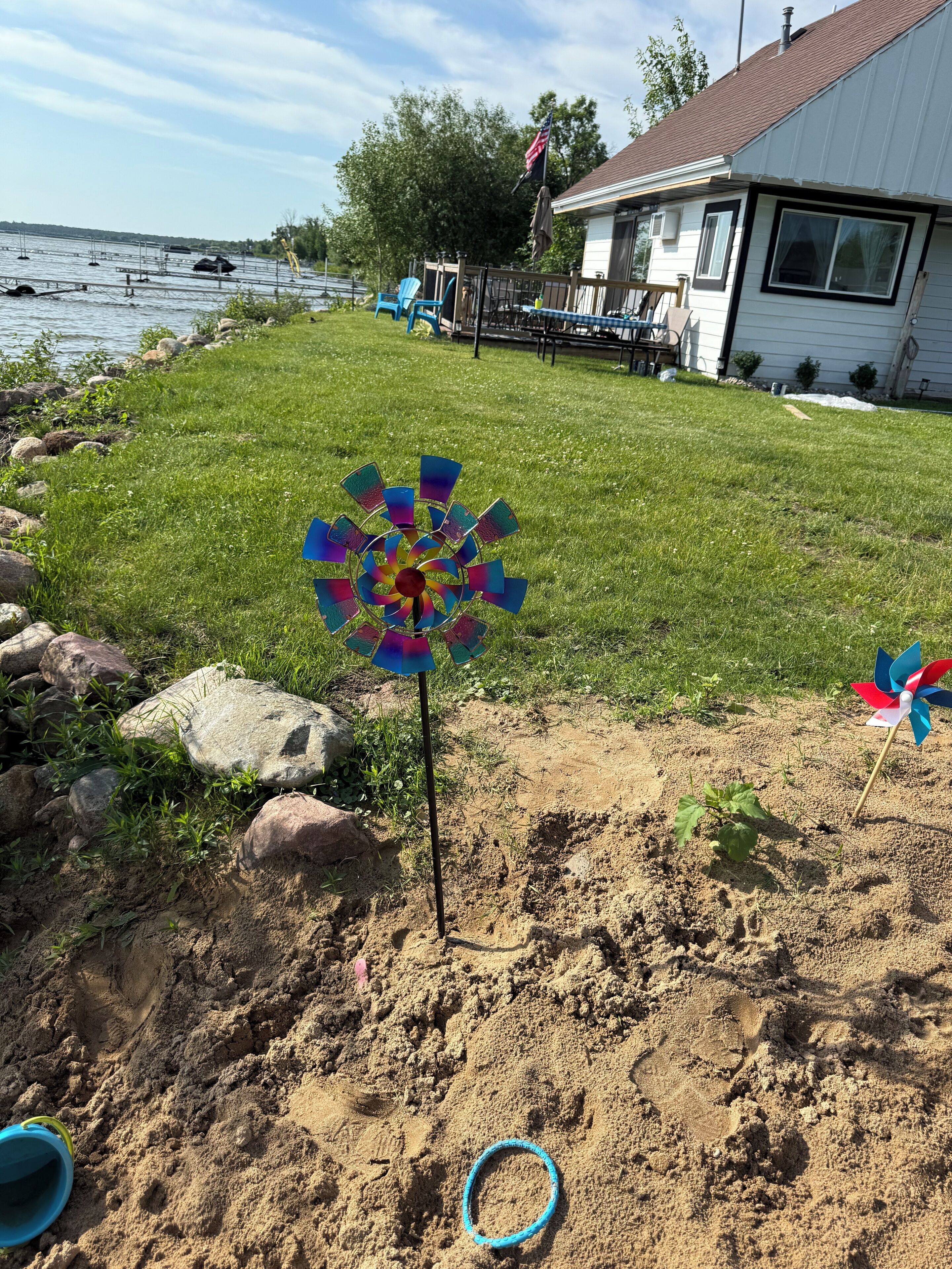 A pinwheel on a grassy area with a house and a body of water in the background.