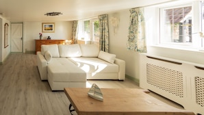 A spacious living room with a large sofa, a wooden coffee table, and a radiator. - Edelweiss | East Ruston Cottages (Happisburgh)