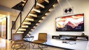 Een moderne woonkamer met een houten trap, twee leren fauteuils, een flatscreen televisie en een boekenkast.