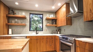 Een moderne keuken met houten kastjes, een inbouwoven en een raam met uitzicht op bomen.