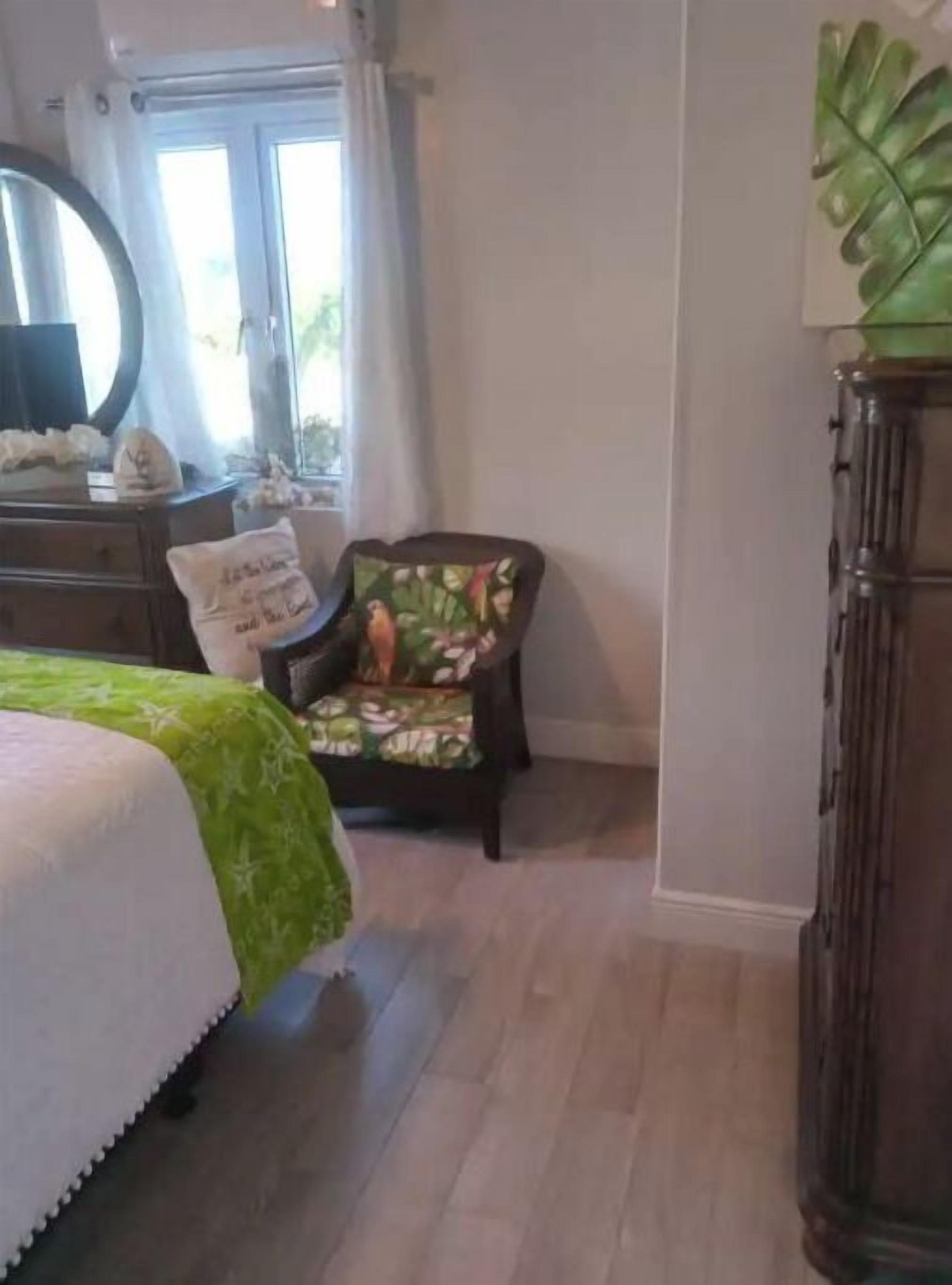 A bedroom with a bed, a chair with a floral cushion, a dresser, and a mirror.