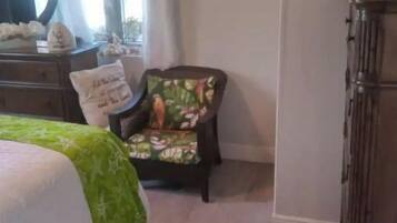 A bedroom with a bed, a chair with a floral cushion, a dresser, and a mirror.