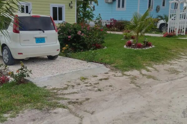 Un coche blanco aparcado en una entrada con un camino de hormigón que lleva a una casa de color azul y una valla blanca.