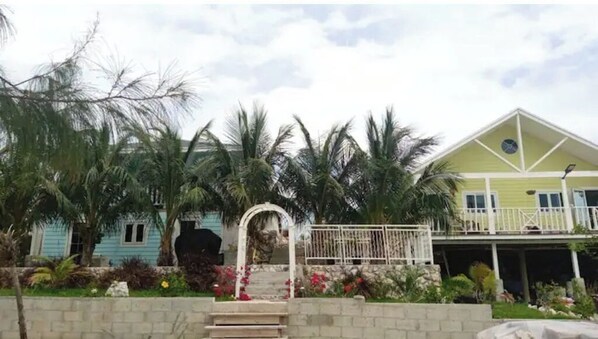 A two-story building with a balcony, surrounded by palm trees and a small garden.