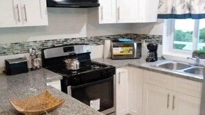 Una cocina con gabinetes blancos, encimera de granito, estufa y cafetera.