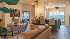 A spacious living room with a leather sofa, grey armchairs, and a dining area with a bar. - Hill Country Guest Retreat Near Wedding Venues, Breweries, & Wineries (Dripping Springs)