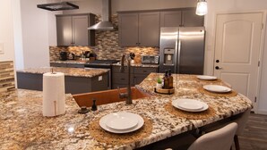 A modern kitchen with granite countertops, stainless steel appliances, and a central island with seating. - Hill Country Guest Retreat Near Wedding Venues, Breweries, & Wineries (Dripping Springs)