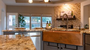 A modern kitchen with granite countertops, stainless steel appliances, a farmhouse sink, and a ceiling fan. - Hill Country Guest Retreat Near Wedding Venues, Breweries, & Wineries (Dripping Springs)