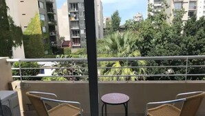 Un balcón con dos sillas de mimbre y una pequeña mesa redonda, con vistas a una zona residencial con edificios y vegetación.