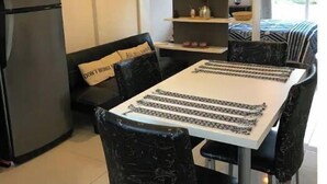 Una cocina moderna con refrigerador, mesa de comedor y sillas. Hay un sofá con cojín y un aparador con adornos.