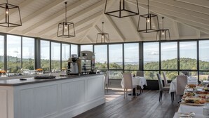 Una cocina amplia con una isla grande, elegantes lámparas colgantes y vistas al exterior a través de amplios ventanales.