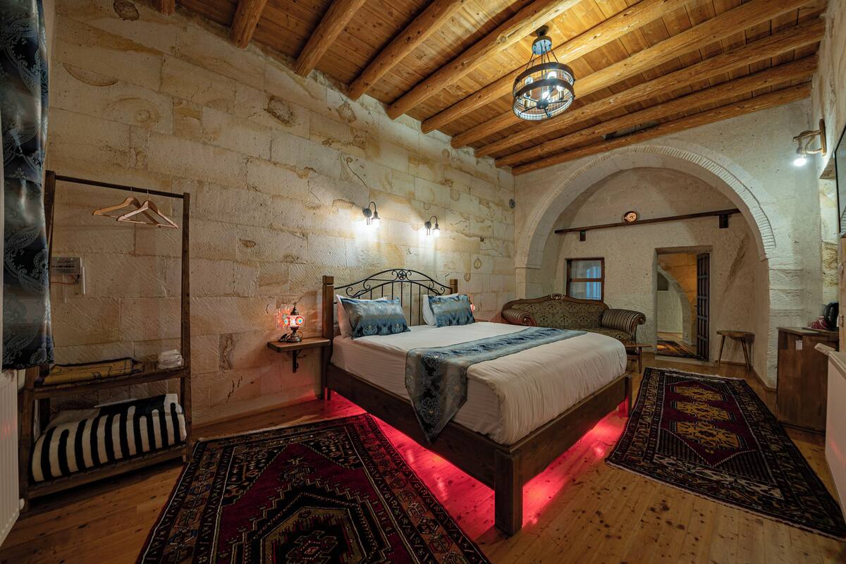 A bedroom with a wooden bed, a hanging wardrobe, and a stone wall.