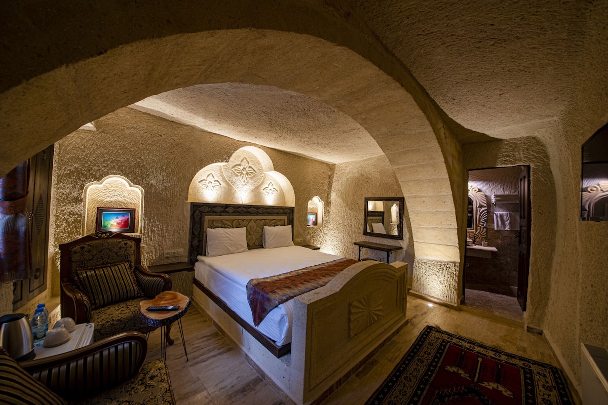 A cozy, stone-walled bedroom with a large bed, a chair, and a small table.