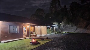 Un edificio moderno de madera con una entrada bien iluminada, un brasero y una zona de patio.