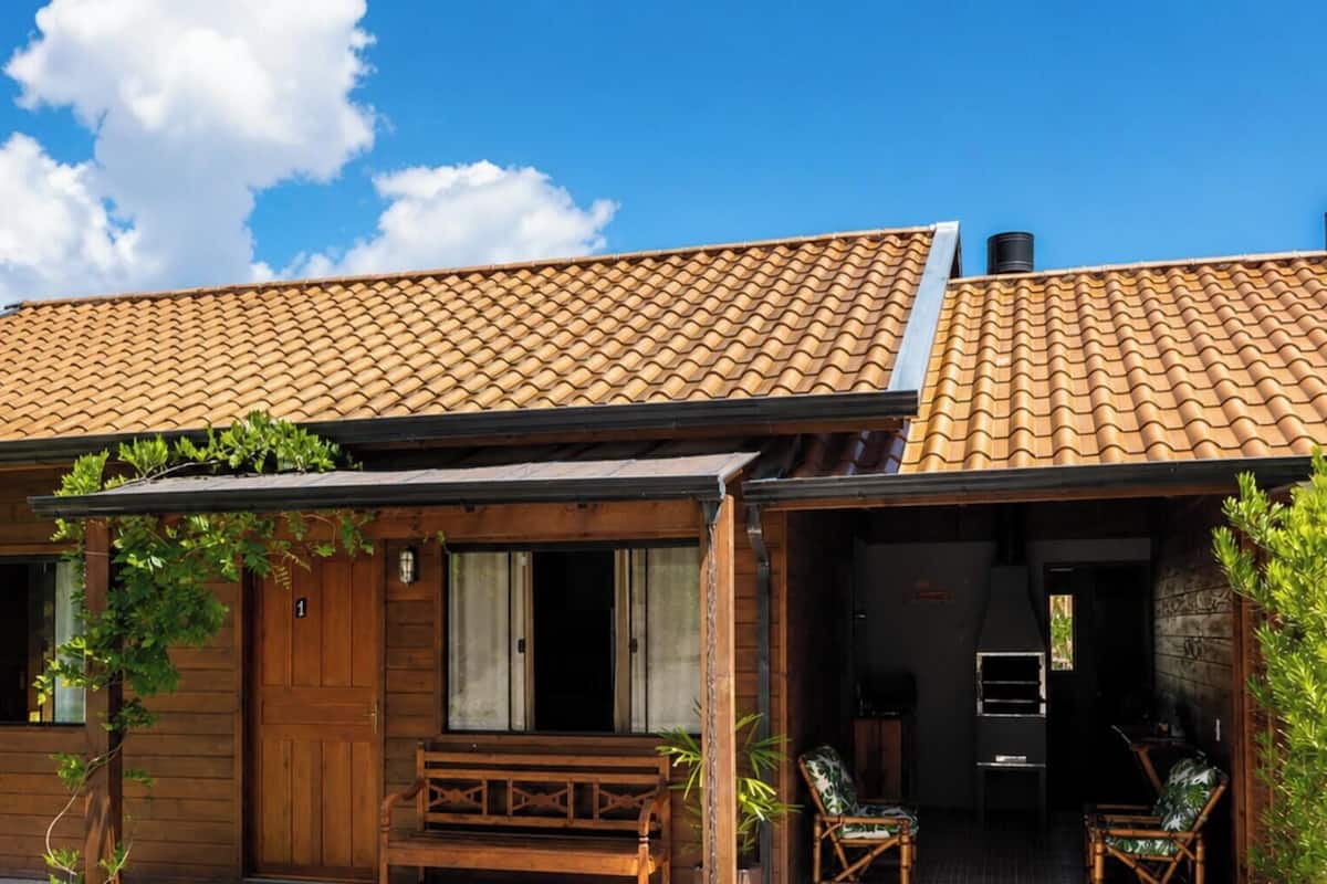 A wooden house with a tiled roof, a front porch with a bench, and a door leading to an interior space.