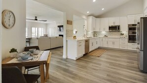Une cuisine moderne avec des meubles blancs, des appareils en acier inoxydable et un coin repas comprenant une table et des chaises en bois.