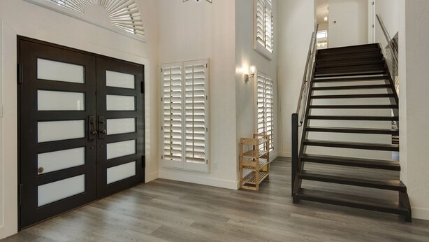 Un hall d’entrée spacieux avec un escalier en bois, une porte de garage double dotée de panneaux en verre dépoli et une lucarne au-dessus.