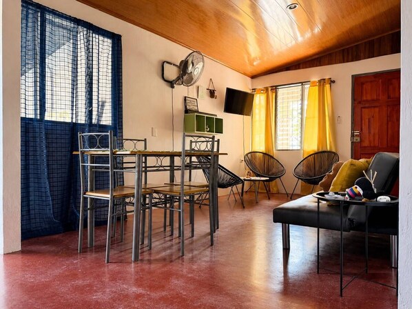 A room with a dining area, seating, a television, and a wooden ceiling.