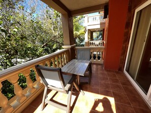 Un balcon avec une table et des chaises, une vue sur des arbres et un bâtiment en arrière-plan.