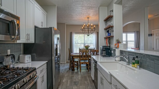 A modern kitchen with white cabinetry, a stainless steel refrigerator, a gas stove, and a chandelier.