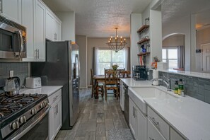 A modern kitchen with white cabinetry, a stainless steel refrigerator, a gas stove, and a chandelier.