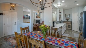 A dining area with a wooden table, chairs, a colorful table runner, and a chandelier.