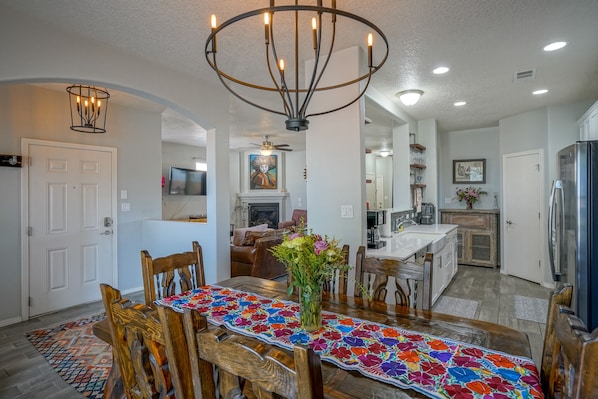 A dining area with a wooden table, chairs, a colorful table runner, and a chandelier.