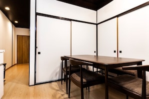 Una habitación con piso de madera, techo oscuro y una pared divisoria blanca con una puerta.