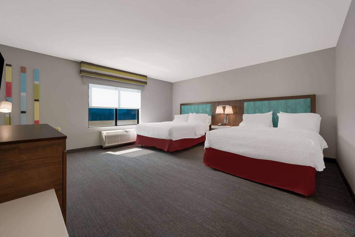 A hotel room with two beds, a desk, a window with a view, and a ceiling with a light fixture.