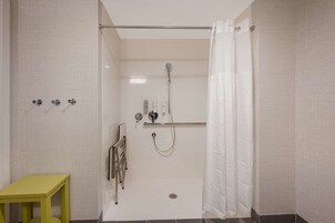Una ducha a nivel con puerta de vidrio, un perchero y una mesita.