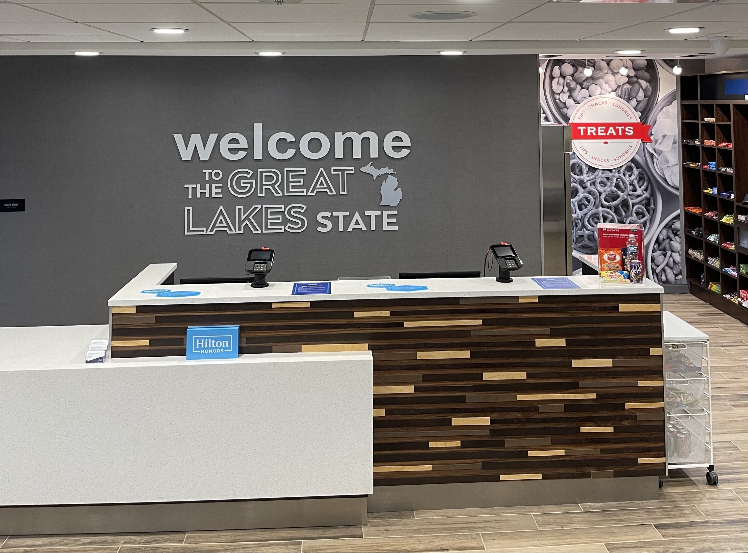 A reception desk with a "Welcome to the Great Lakes State" sign, a "Hilton Honors" sign, and a "Treats" sign with snacks.