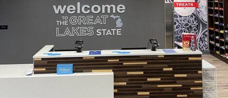 A reception desk with a "Welcome to the Great Lakes State" sign, a "Hilton Honors" sign, and a "Treats" sign with snacks.
