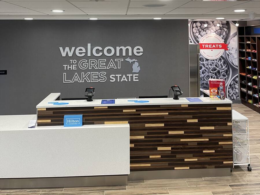 A reception desk with a "Welcome to the Great Lakes State" sign, a "Hilton Honors" sign, and a "Treats" sign with snacks.