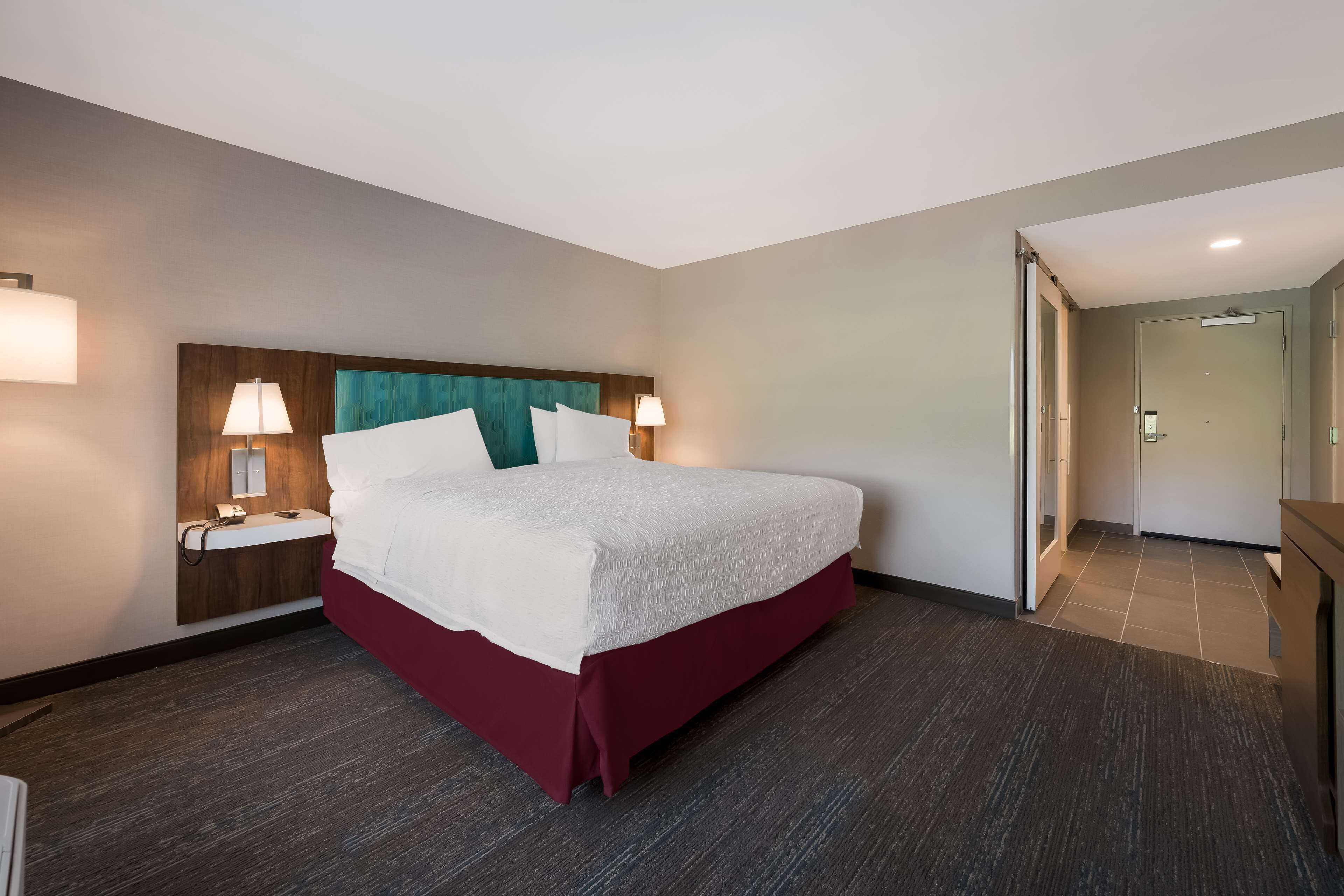 Habitación de hotel con una cama grande, dos lámparas de noche, una mesita de noche y un cabecero de madera.