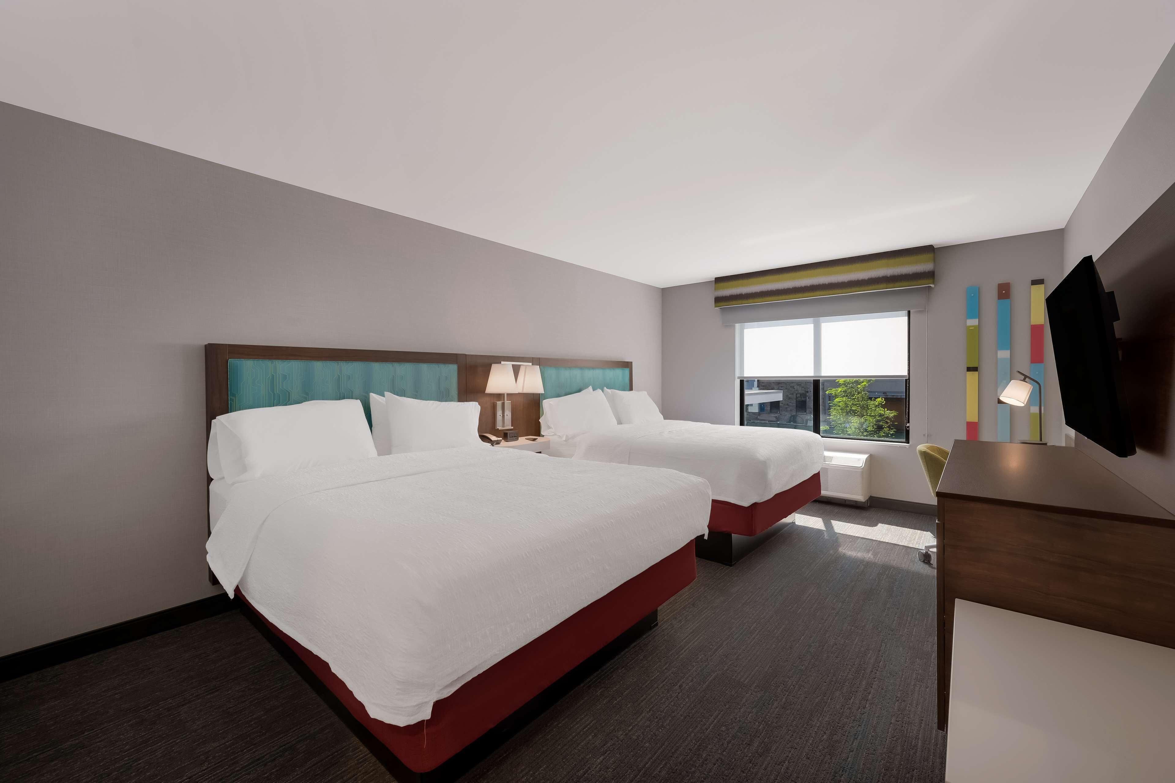 A hotel room with two beds, a desk, a chair, and a large window with a view.