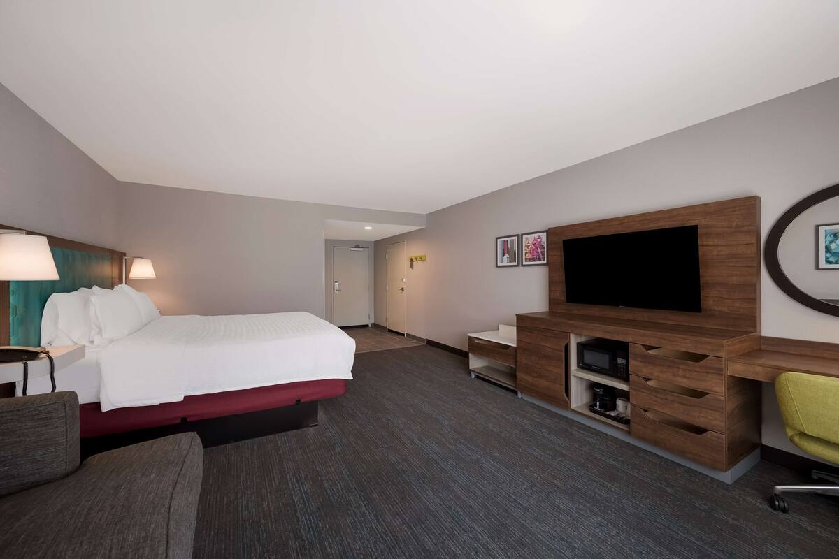 A hotel room with a bed, a desk, a chair, a TV, and a TV stand.