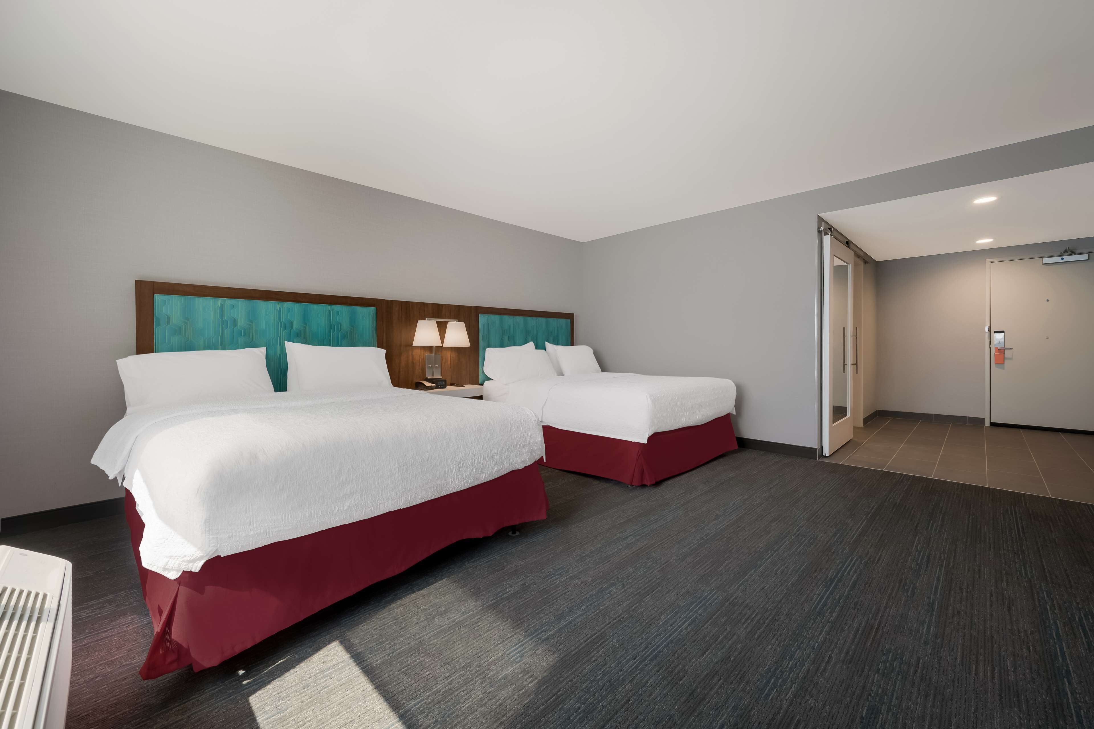 A hotel room with two beds, a wooden headboard, and a red skirted bed.