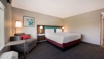 A hotel room with a bed, bedside tables, a desk, a chair, and a wall-mounted artwork.