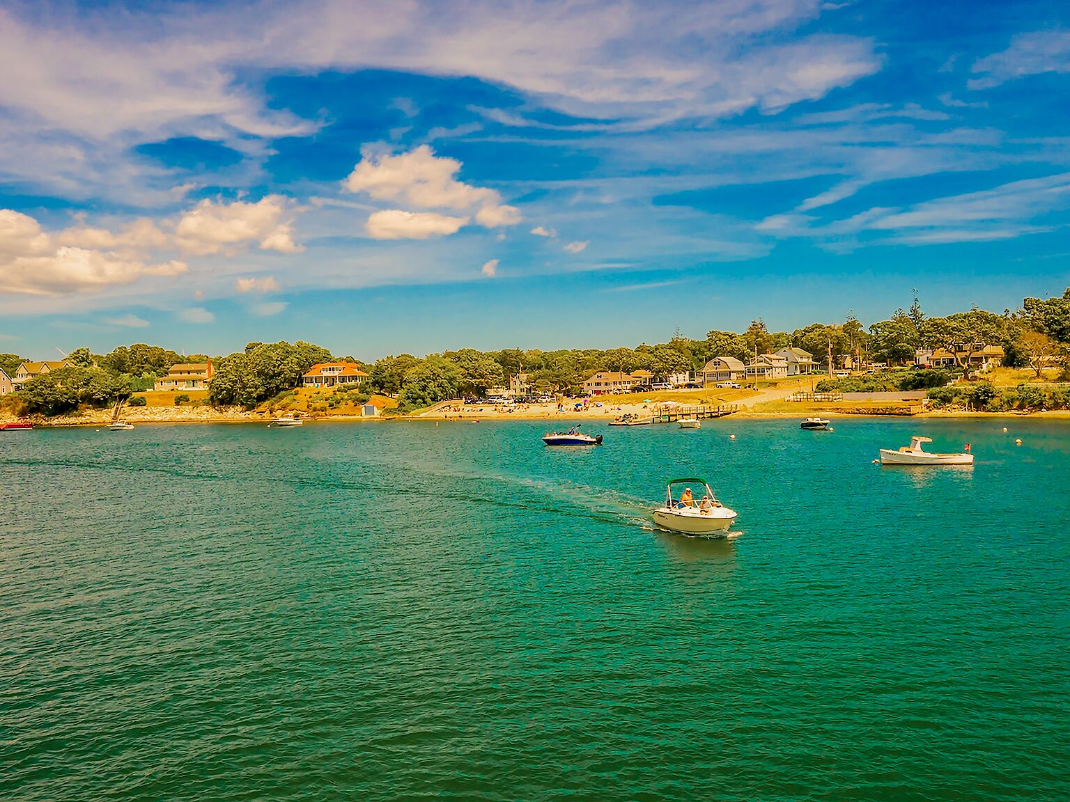 A coastal view with boats on the water, a sandy beach, and houses along the shore.