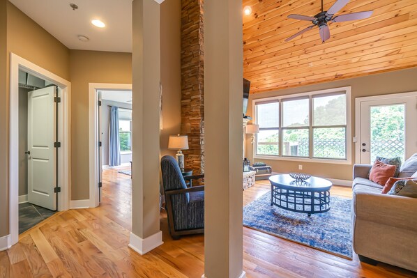 A spacious living area with a stone accent wall, a ceiling fan, and a large window with a view of greenery. - The Getaway at Center Hill Lake (Silver Point)