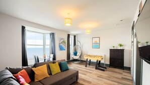 Een moderne woonkamer met een bank, een tafelvoetbalspel en uitzicht op zee.